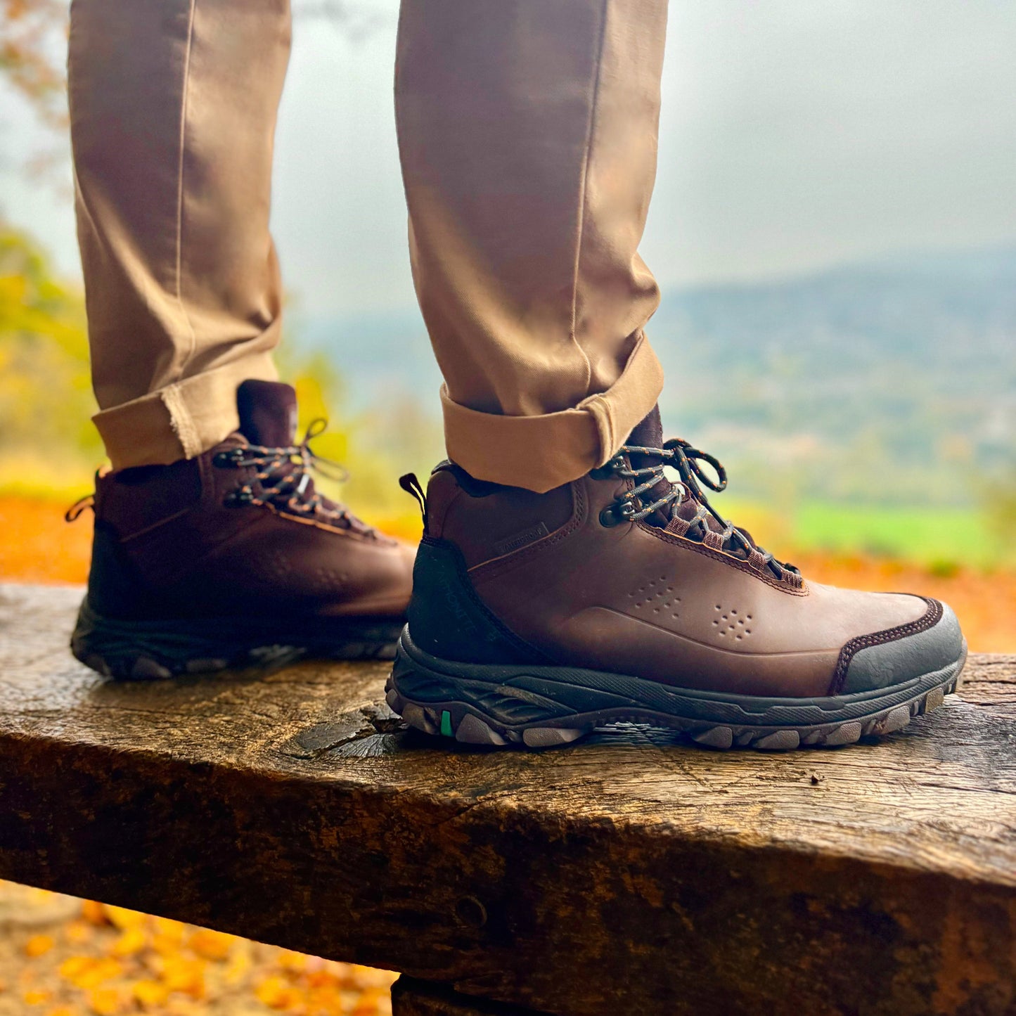 Brown hiking boots with laces on a wooden bench in an outdoor setting with blurred background