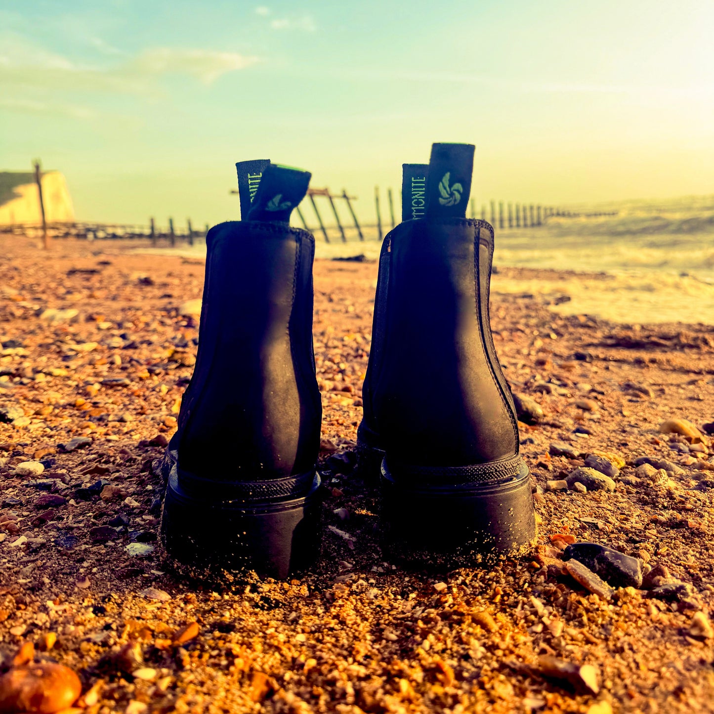 Black Chelsea boots for women on a sandy beach with the sea in the background