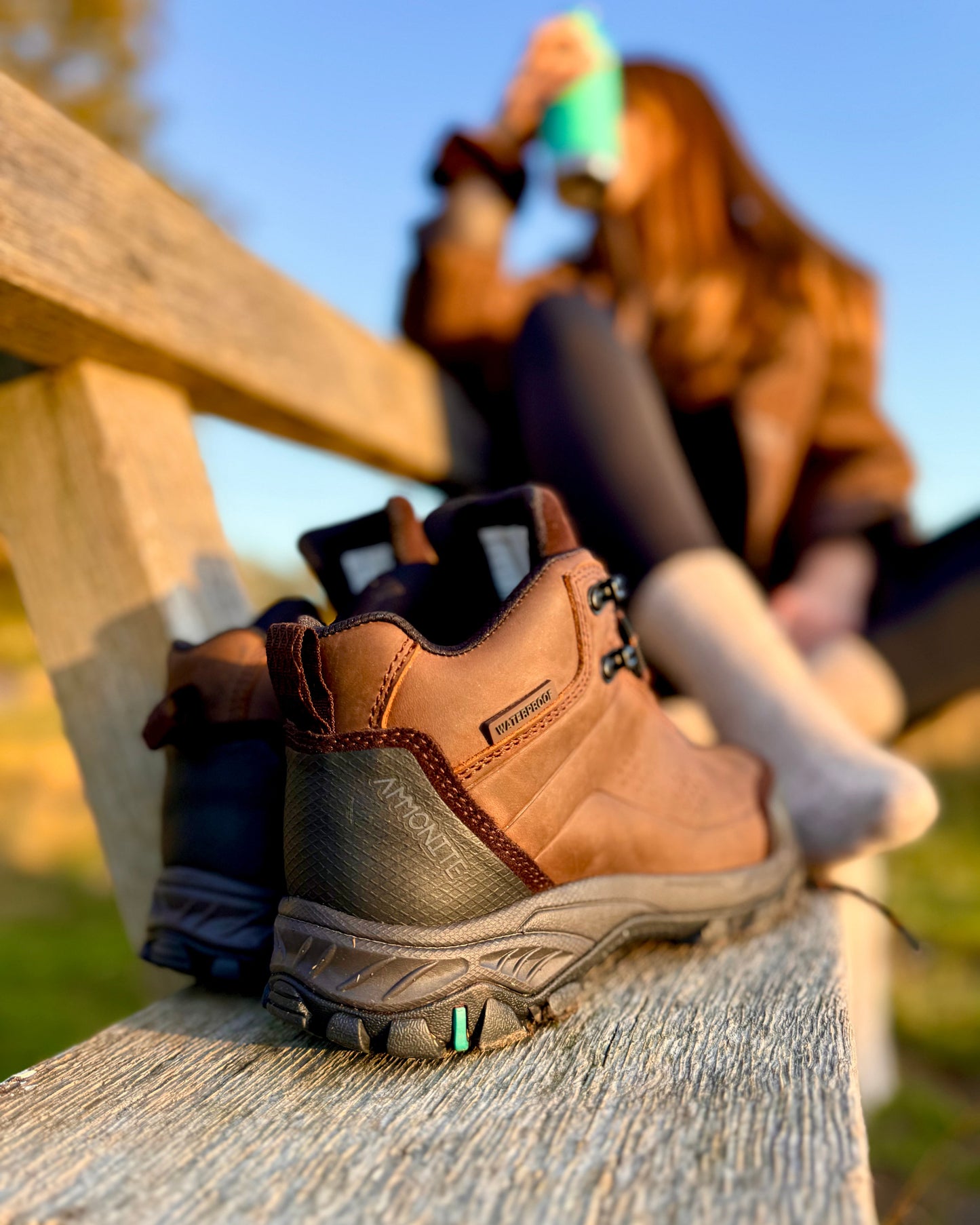 Brown runswick hiking boots on a wooden bench with a blurred person in the background
