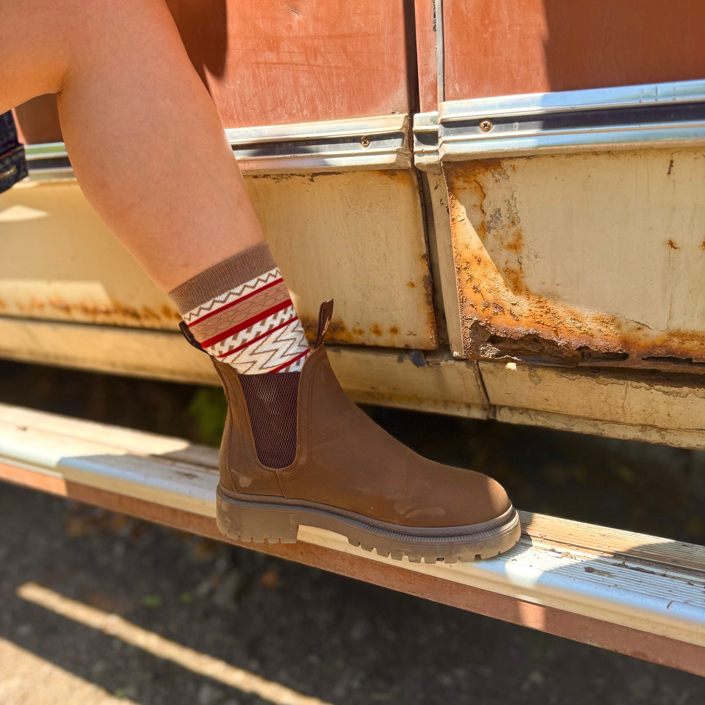 Woman wearing brown chelsea boots and patterned socks on a vehicle.