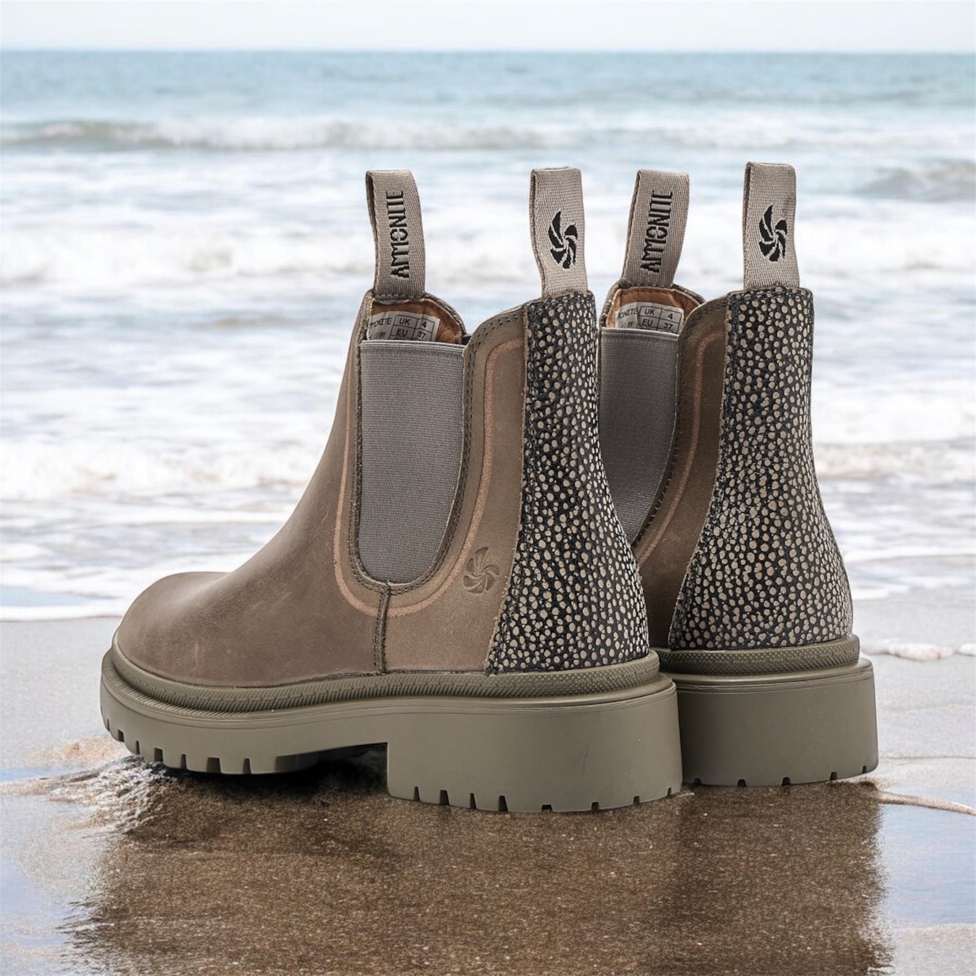 Pair of Grey Chelsea boots with decorative pattern on a beach.